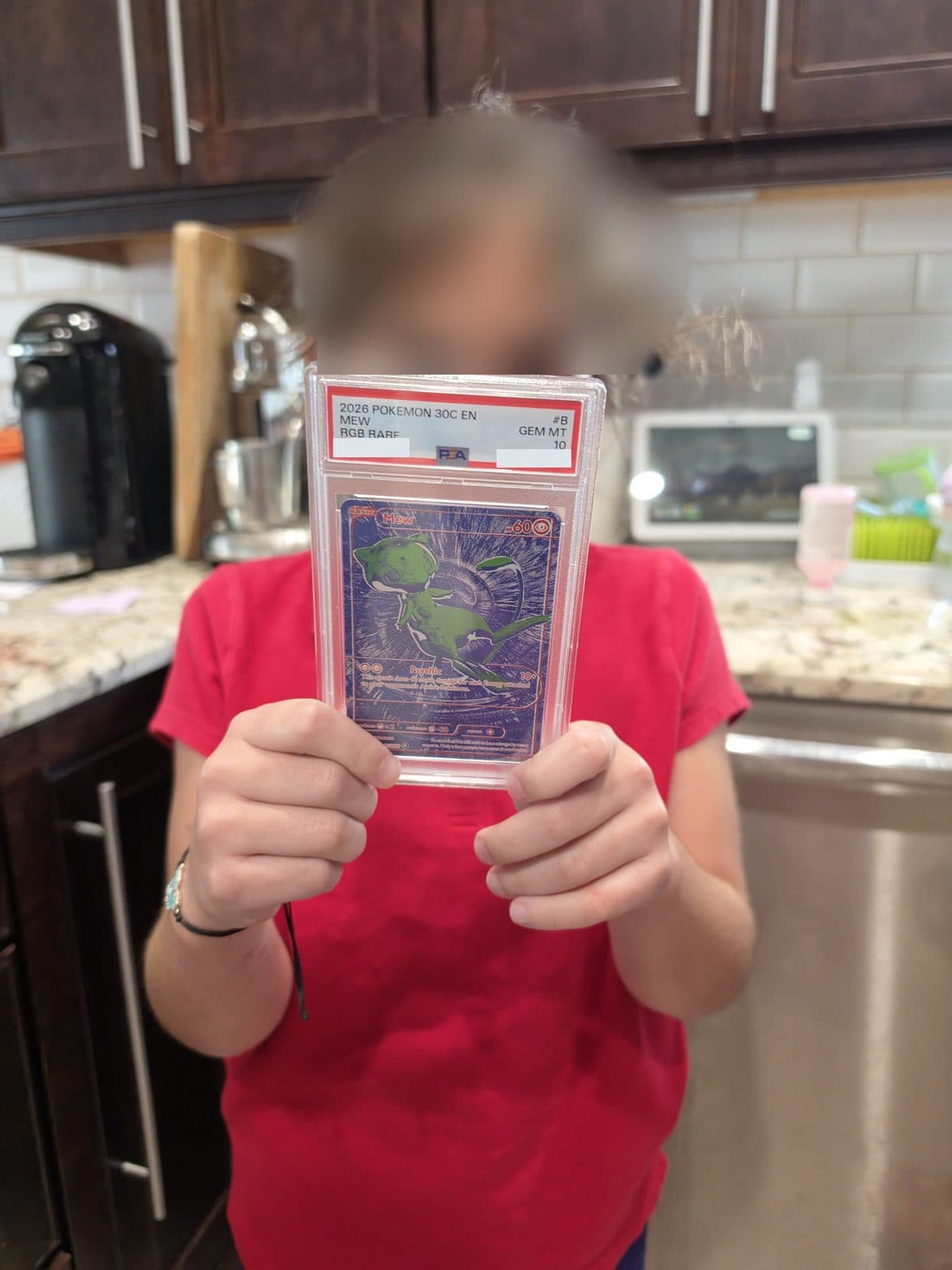 Lila holding the PSA 10 B/RGB Mew slab in the kitchen, her face blurred