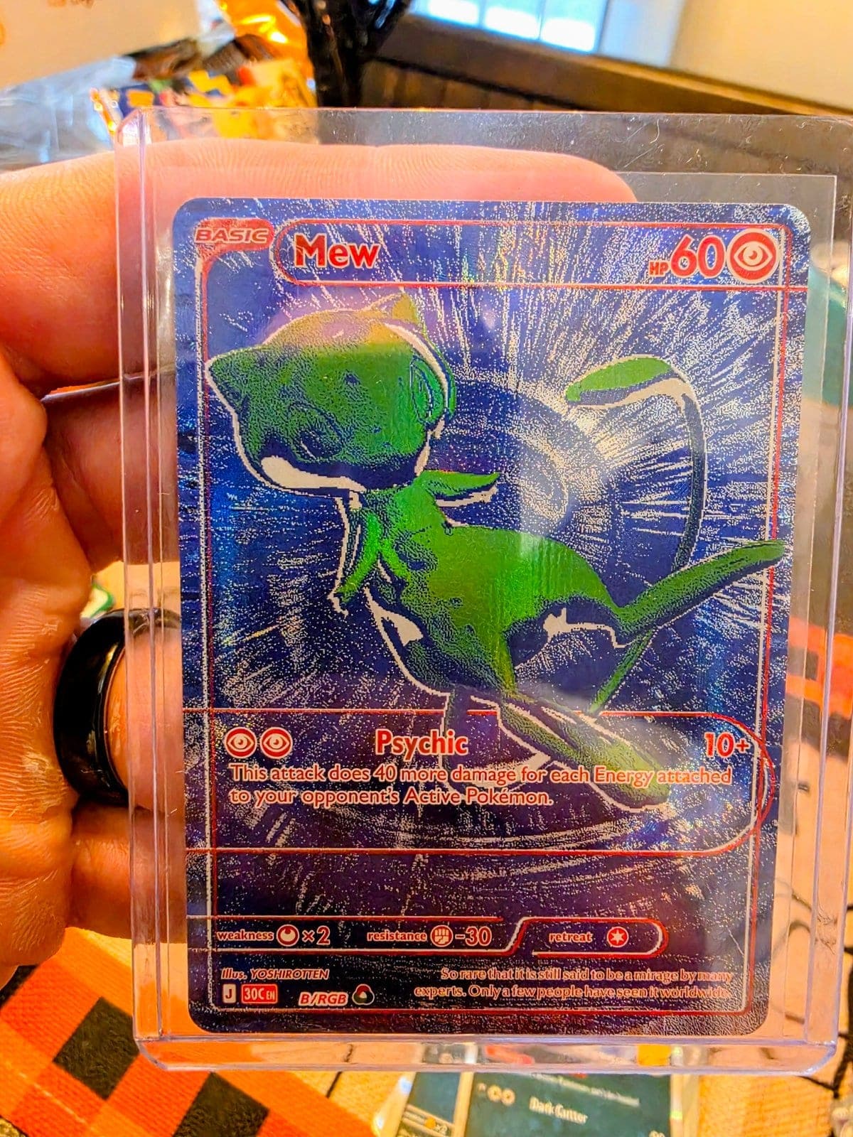 The Mew B/RGB card in a top loader, held in a hand at home